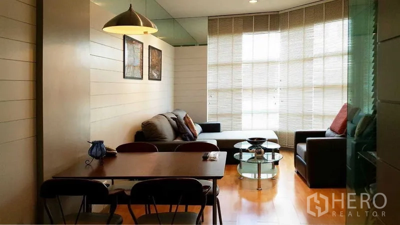 Condominium for rent in Khlong Toei, Bangkok - Dining and lounge area with bay window, round glass table and sectional sofa.