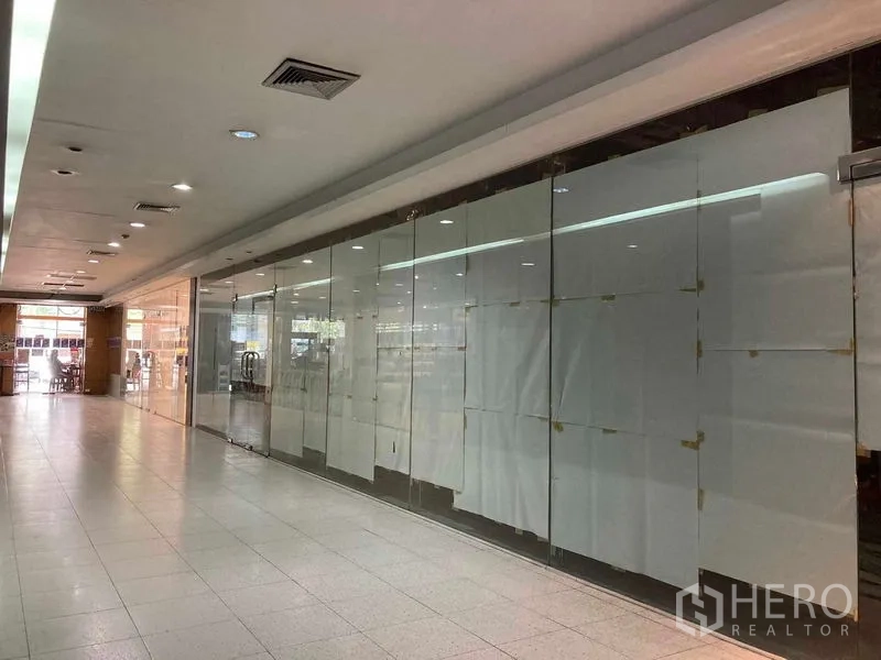 Retail Space for rent - Glass-walled retail unit facing a bright arcade with suspended ceiling lights and polished tile flooring.