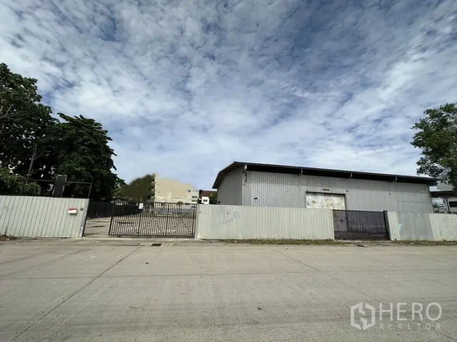 货栈 出租在Min Buri, Bangkok - 街景：带金属围栏的工业用地入口，灰色仓库外观，位于Min Buri。