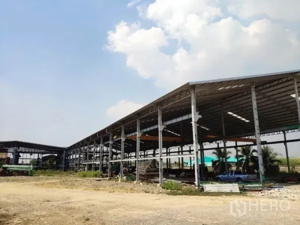 Factory for rent in Samut Sakhon - Side view of long steel-frame warehouse with open bays and a gravel yard in Bang Krachao.