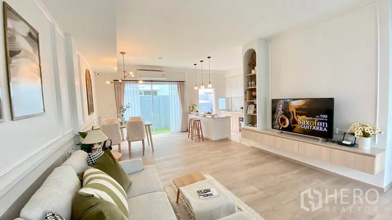 Townhouse for rent in Prawet, Bangkok - Bright open-plan living, dining and kitchen with light wood floors, built-in TV wall and sliding doors to the patio.
