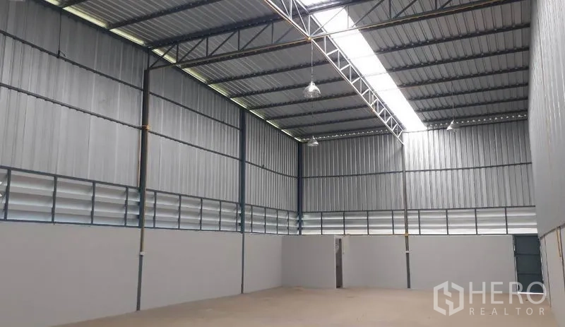 Warehouse for rent in Mueang Pathum Thani, Pathum Thani - High-ceiling metal warehouse interior in Mueang Pathum Thani with skylight strip, ventilation louvers and smooth concrete floor.