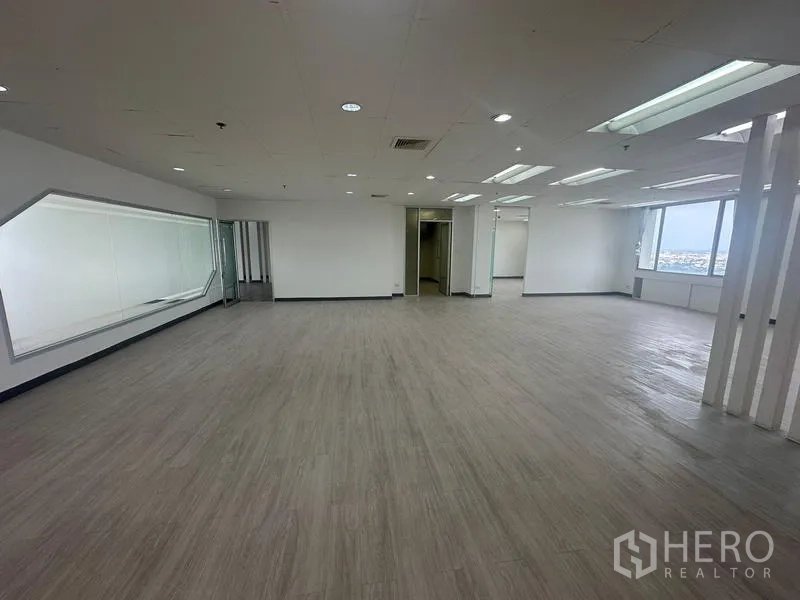 Office Space for rent - Expansive office floor with LED ceiling lights, slatted partitions, and large windows overlooking Bangkok.