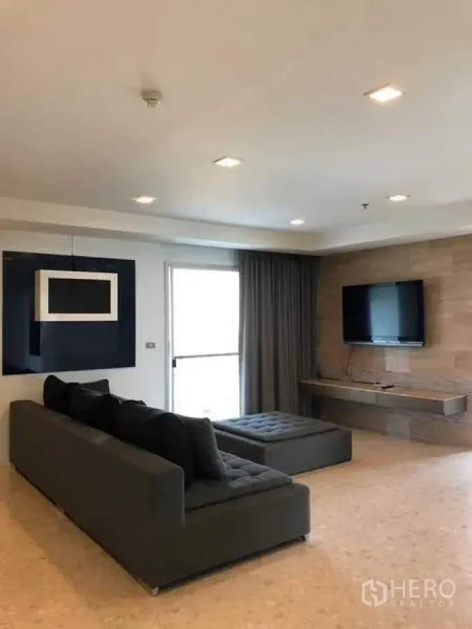 Condominium for rent in Khlong Luang, Pathum Thani - Living room with gray sectional sofa and wall-mounted TV unit.