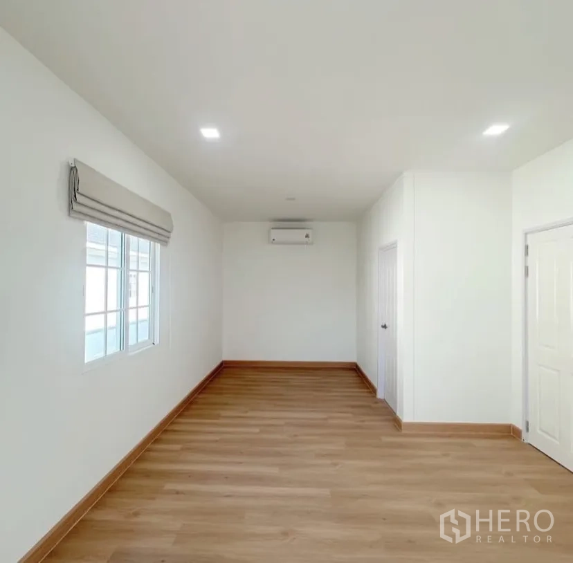 Detached House for rent in Mueang Samut Prakan, Samut Prakan - Long multipurpose room with wood floors, white walls and air conditioning.
