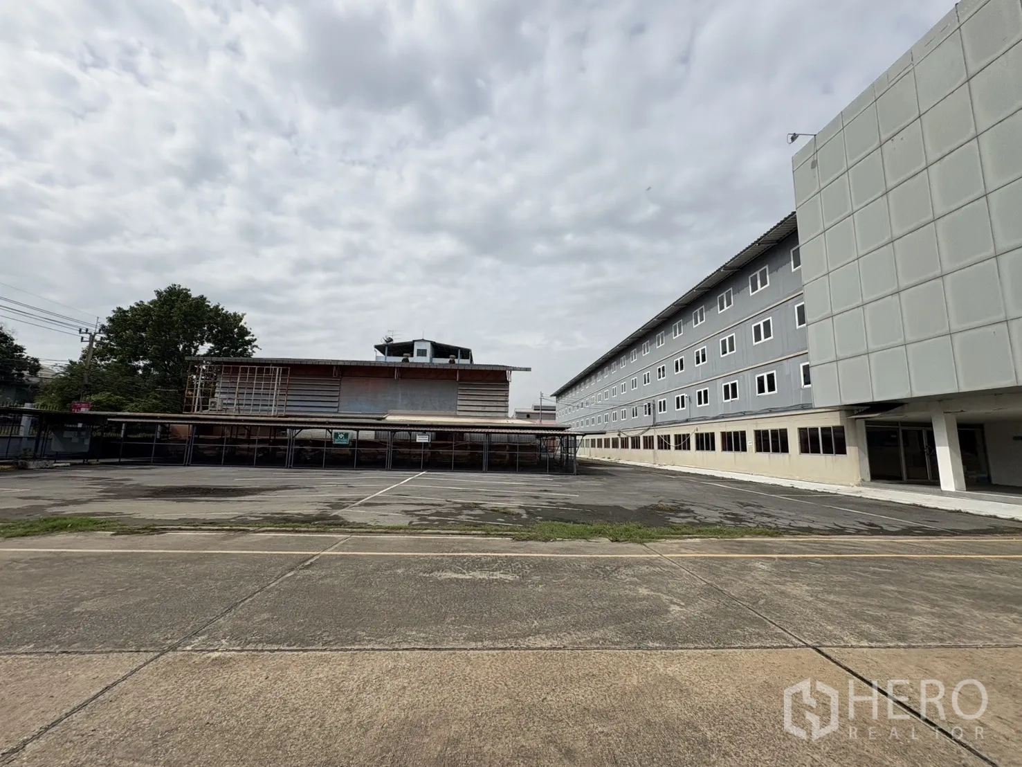 Factory for rent in Phra Pradaeng, Samut Prakan - Large paved yard and parking beside a multi‑storey office block.