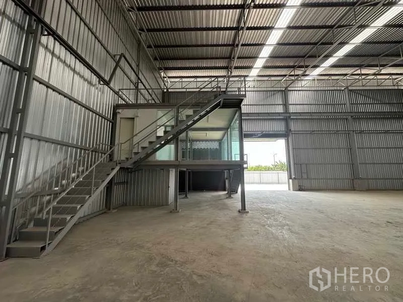 Factory for rent in Wang Noi, Phra Nakhon Si Ayutthaya - Spacious warehouse interior with high ceiling, skylight strips, and a mezzanine glass office accessed by steel stairs.
