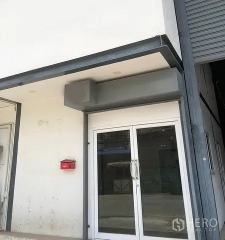 Warehouse for rent in Pak Kret, Nonthaburi - Front entrance with double glass doors next to a large roller shutter.