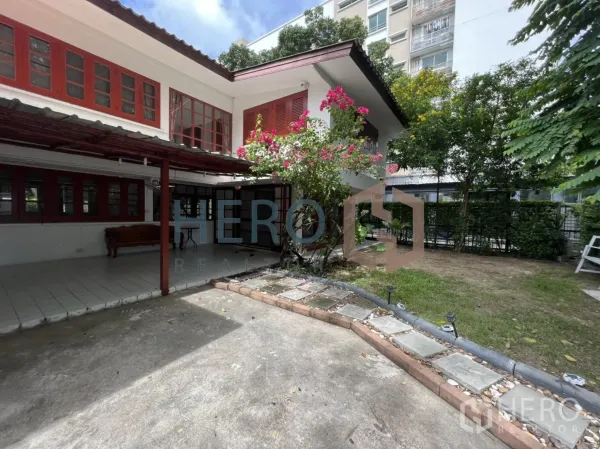 Detached House for rent in Watthana, Bangkok - House exterior with bougainvillea, paved driveway and a nearby mid-rise building.