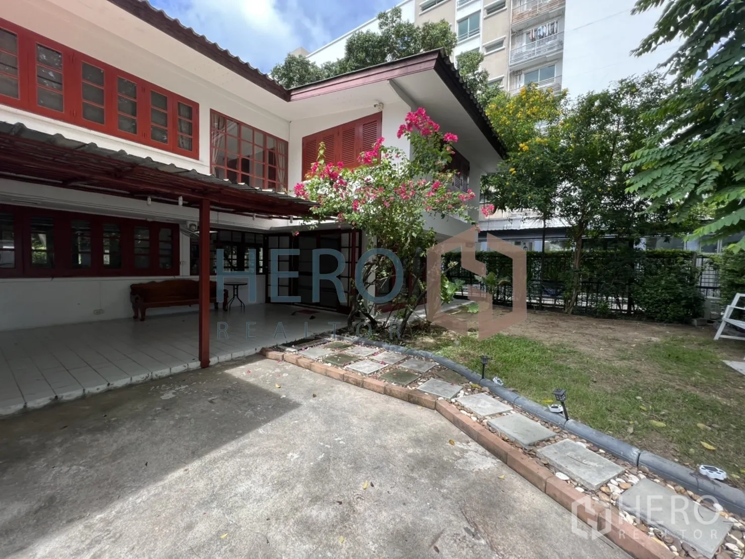 Detached House for rent in Watthana, Bangkok - House exterior with bougainvillea, paved driveway and a nearby mid-rise building.