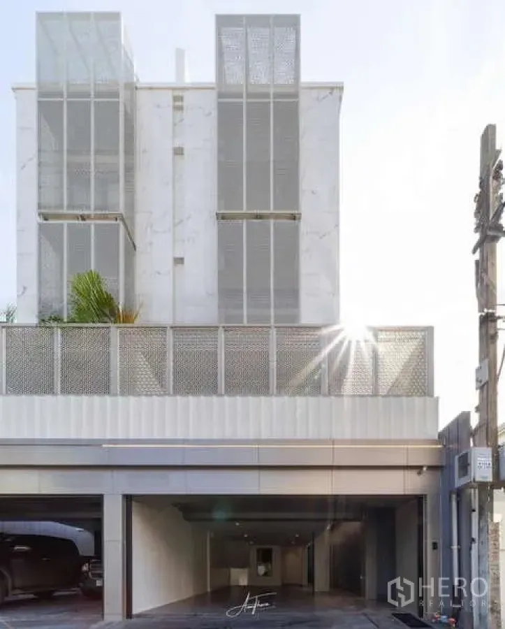 联排别墅 出租或出售在Watthana, Bangkok - 当代联排别墅正立面，带闸门停车位与阳光光晕。