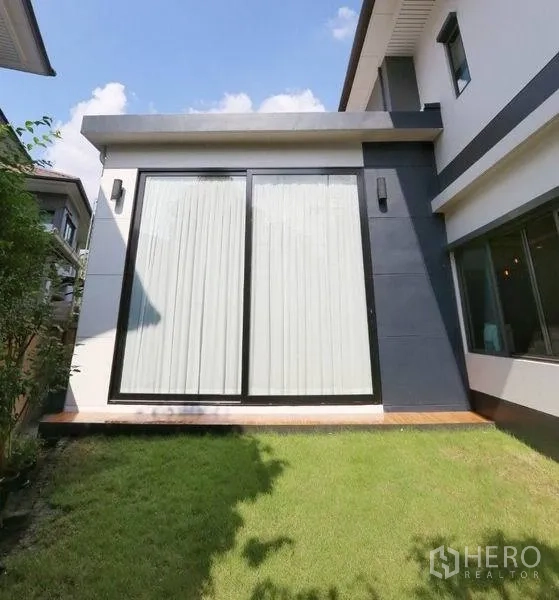 Detached House for rent or sale in Bang Kapi, Bangkok - Private side lawn with floor-to-ceiling sliding glass doors and dark exterior cladding.
