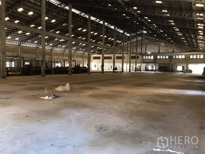 Warehouse for rent in Phra Pradaeng, Samut Prakan - Open warehouse floor facing mezzanine office windows under a steel beam ceiling.