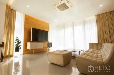 联排别墅 出租在Huai Khwang, Bangkok - 客厅采光充足，配大屏电视、现代沙发与整面高窗帘。