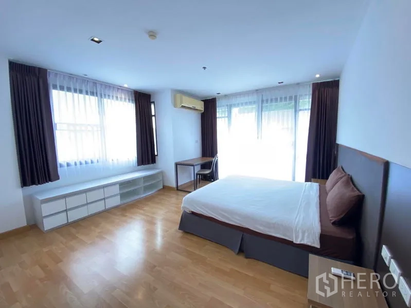 Condominium for rent in Khlong Toei, Bangkok - Spacious bedroom with king bed, desk and wide windows on wood flooring.