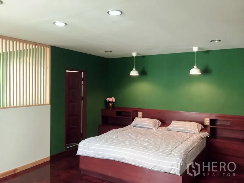 Townhouse for rent in Watthana, Bangkok - Spacious bedroom with green accent wall and built-in wood headboard.