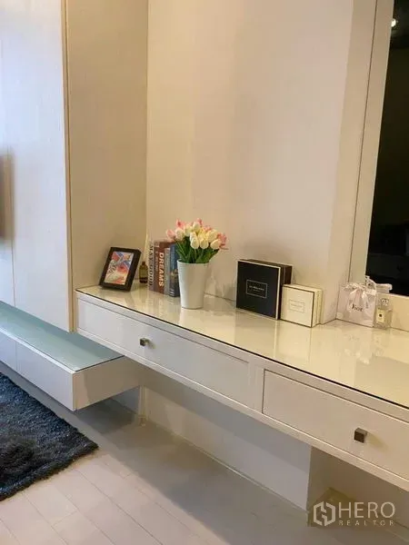Condominium for sale in Pathum Wan, Bangkok - Built-in white vanity with drawers, mirror and flowers in a modern condo bedroom.