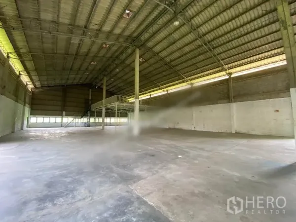 Warehouse for rent in Khlong Sam Wa, Bangkok - Open-plan storage area with ventilated windows, high ceiling, and mezzanine walkway over durable concrete flooring.