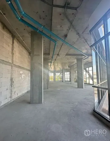 Retail Space for rent in Phra Khanong, Bangkok - Unfitted retail interior with high concrete ceiling, exposed blue piping, columns, and floor-to-ceiling corner windows.