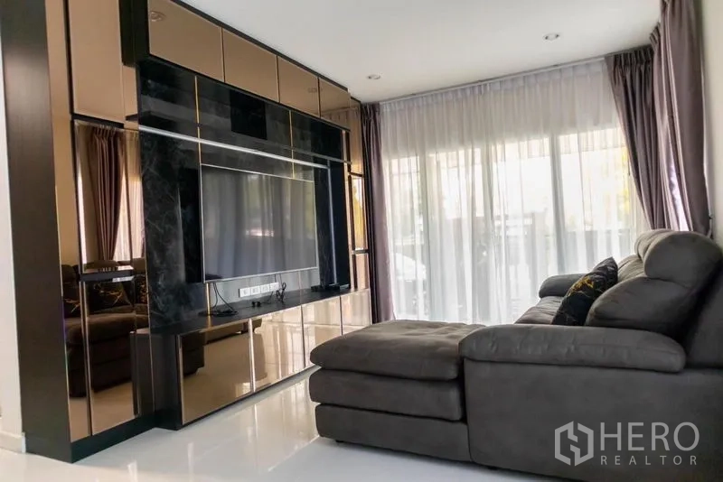 Detached House for rent - L-shaped sectional sofa facing a built-in TV wall with sheer curtains to the patio