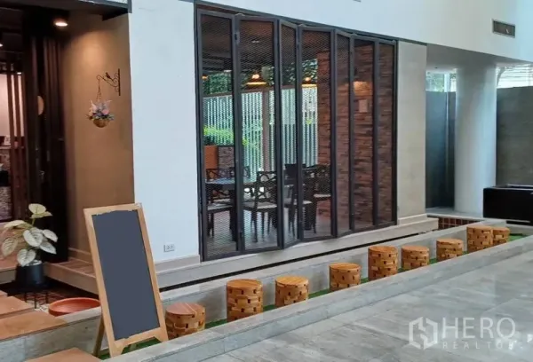 Retail Space for rent in Khlong Toei, Bangkok - Modern retail storefront with folding glass doors, brick accent wall, and wooden stools along a raised walkway.