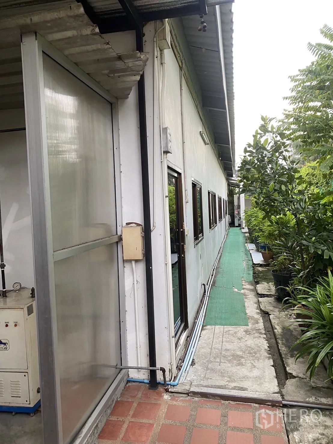 Factory for rent in Prawet, Bangkok - Exterior service walkway beside the factory with green matting and lush plants.