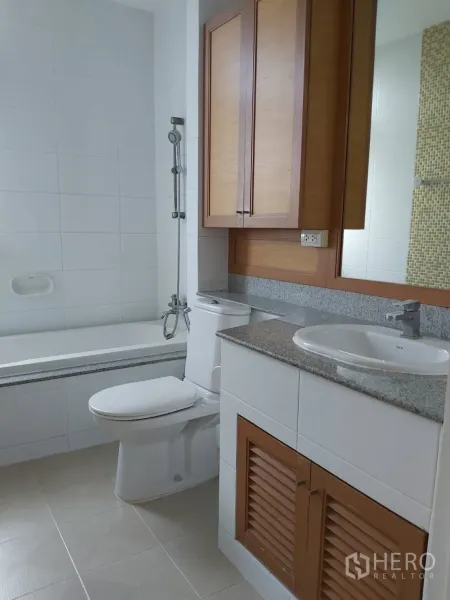 Apartment for rent in Khlong Toei, Bangkok - Bathroom with bathtub and shower combo, toilet, granite vanity, and wood storage cabinets.