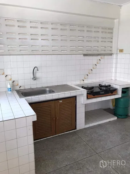 Townhouse for rent in Khlong Toei, Bangkok - White-tiled Thai kitchen with sink, gas hob and ventilation blocks.