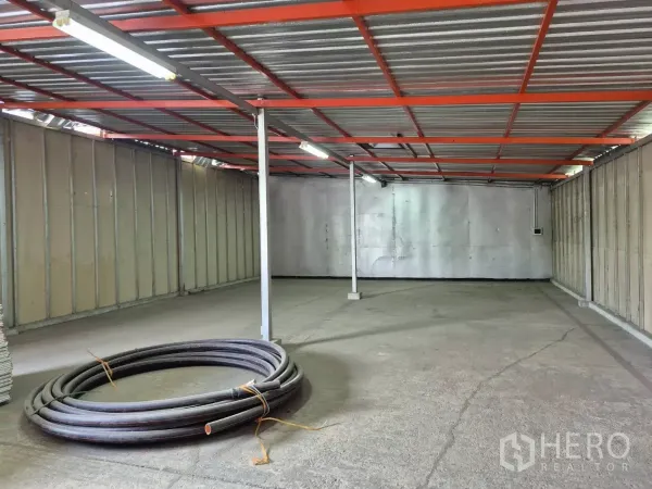 Warehouse for rent in Mueang Pathum Thani, Pathum Thani - Open-plan warehouse interior featuring a concrete floor, red steel roof frame and fluorescent strip lighting.