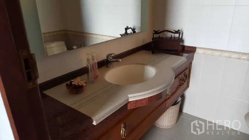 Townhouse for rent in Khlong Toei, Bangkok - Bathroom vanity with stone countertop, large mirror and wooden cabinet.