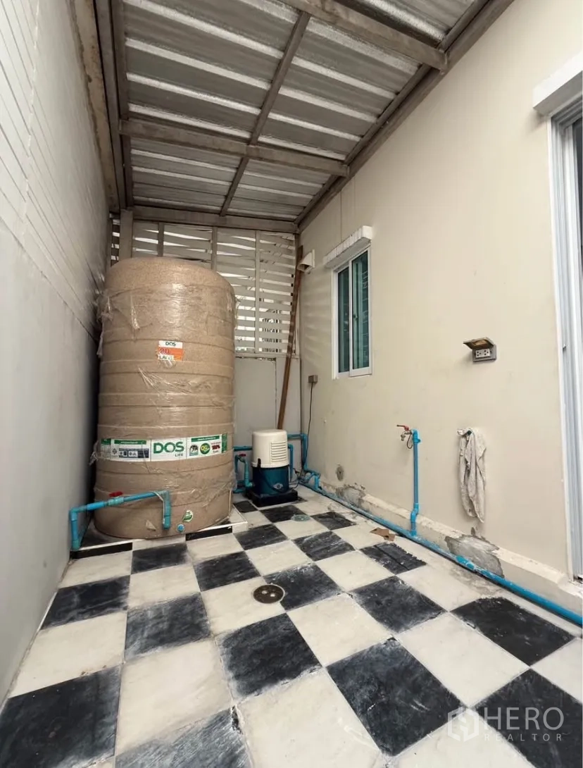 Townhouse for rent in Suan Luang, Bangkok - Rear utility zone with water tank, pump and checker tiles under roof.