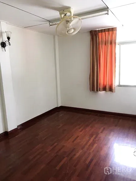 Townhouse for rent in Khlong Toei, Bangkok - Sunny bedroom with polished wooden flooring and orange curtains.