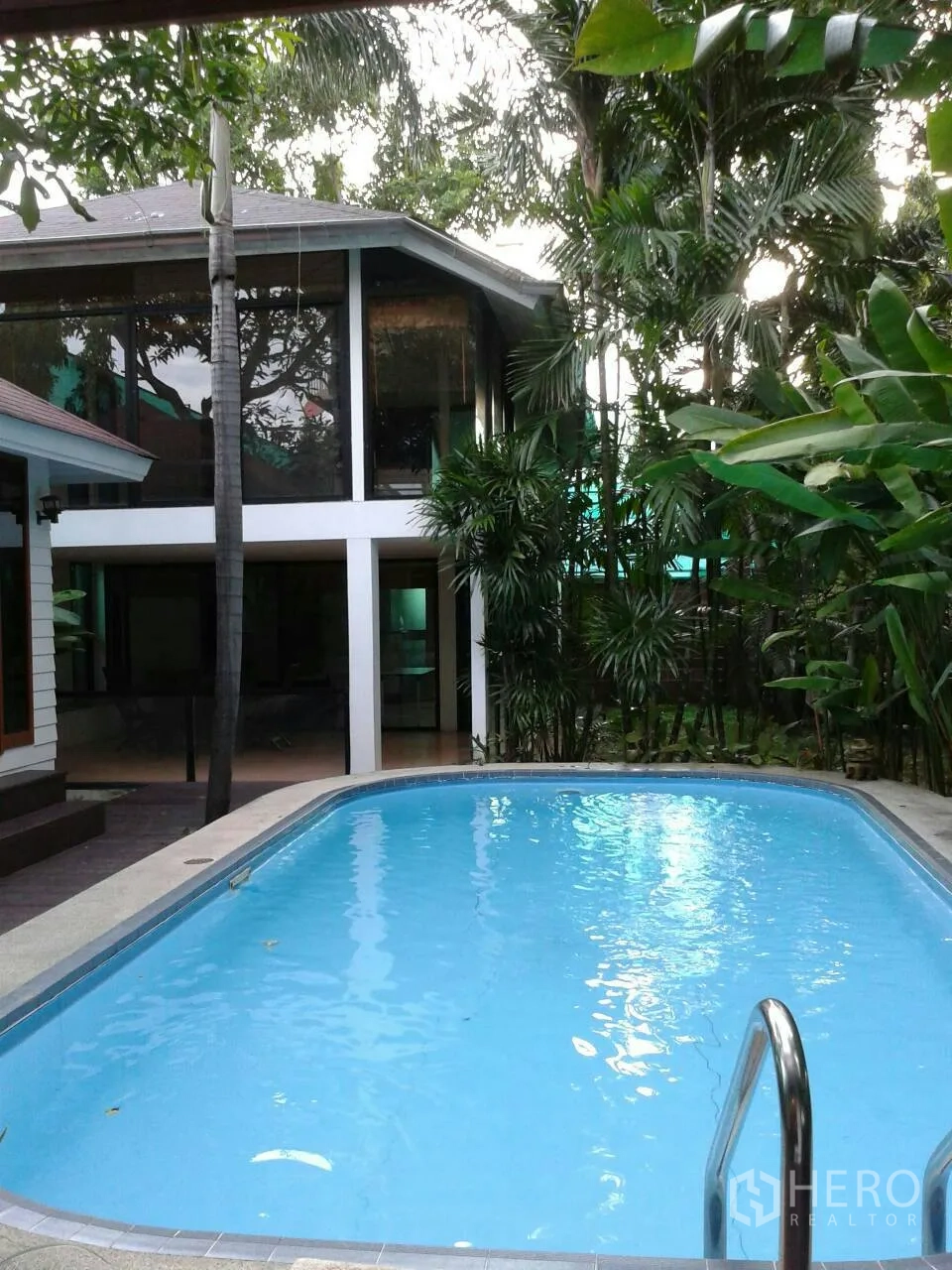Detached House for rent in Suan Luang, Bangkok - Tropical private swimming pool beside a glass-walled detached house surrounded by palms.