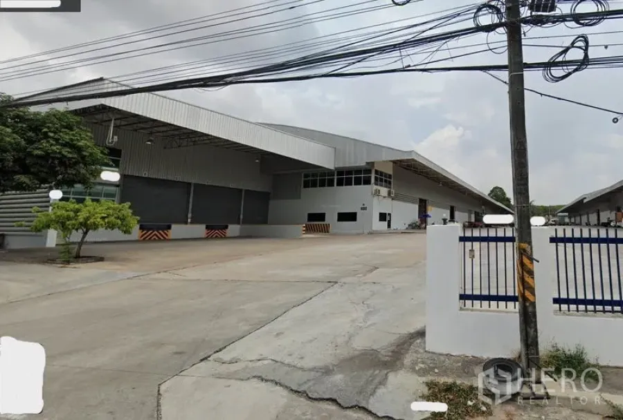 Warehouse for rent in Si Racha, Chon Buri - Modern industrial warehouse exterior in Si Racha, Chon Buri with covered loading docks, wide concrete yard, and gated entrance.