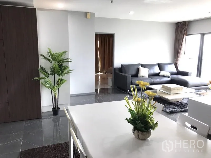 Condominium for rent in Khlong Toei, Bangkok - Open-plan living and dining area with leather sofa and large windows.