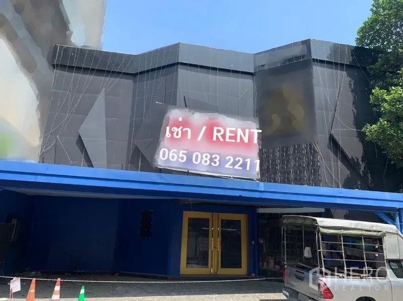 Shophouse for rent in Watthana, Bangkok - Modern black shophouse facade with a blue canopy, gold-framed doors, and a for-rent banner.