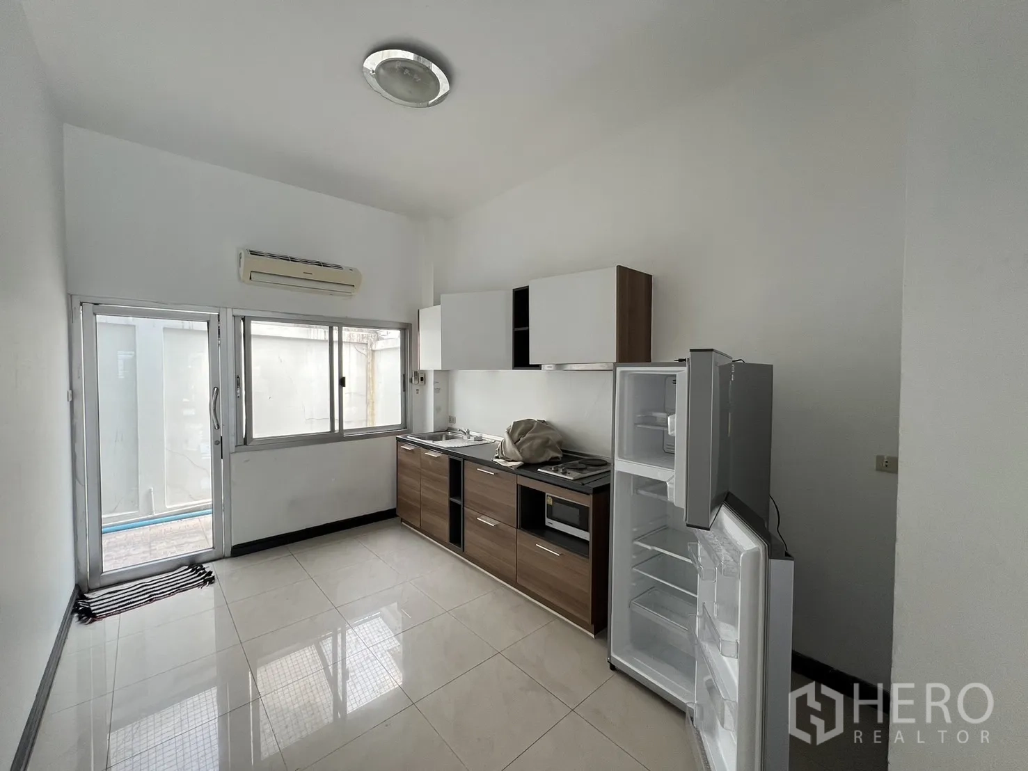 联排别墅 出租在Khlong Toei, Bangkok - 配备橱柜、灶台、水槽和打开的冰箱的厨房，临玻璃门。