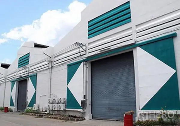 Warehouse for rent in Prawet, Bangkok - Row of warehouse bays with teal-and-white accents, multiple roller shutter doors and service area.