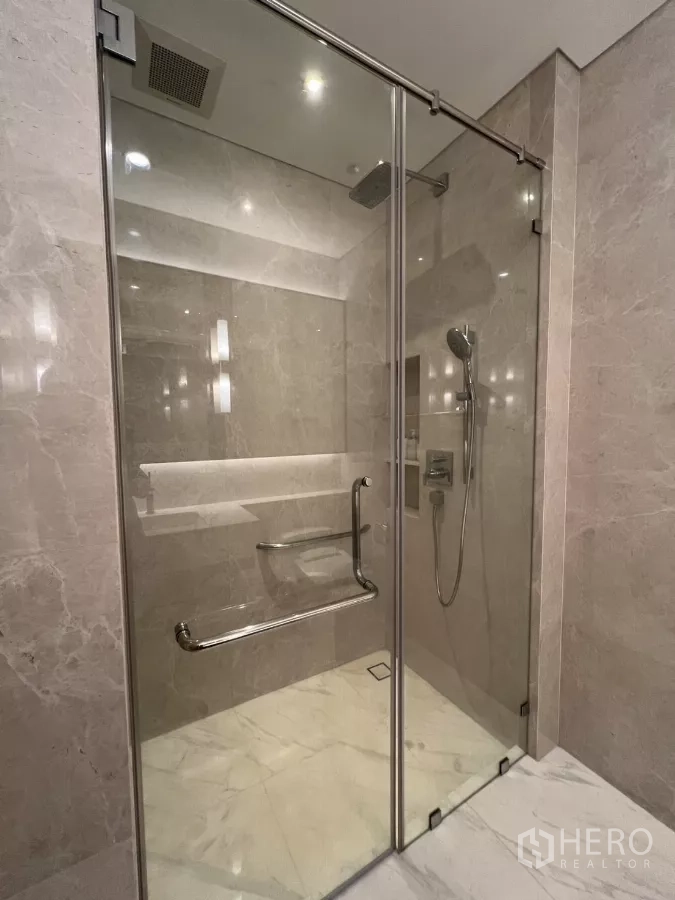 Condominium for rent in Pathum Wan, Bangkok - Glass-enclosed shower with rain showerhead and bench inside a marble bathroom.