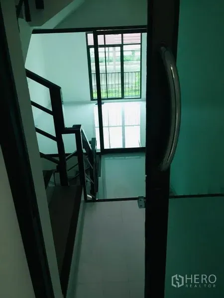 Home Office for rent in Wang Thonglang, Bangkok - View down the stairwell through a glass door toward a sunlit window and balcony rail.