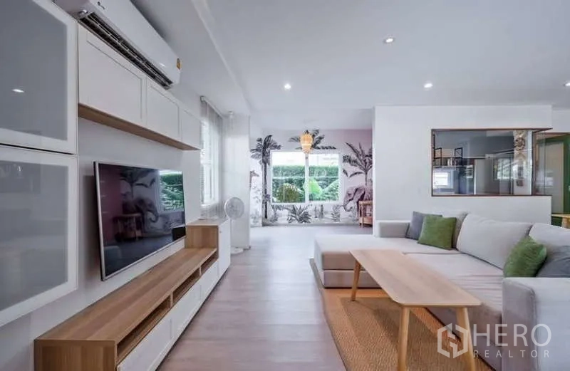 Detached House for rent in Prawet, Bangkok - Open-plan lounge and dining space with large sofa, feature wall and garden outlook.
