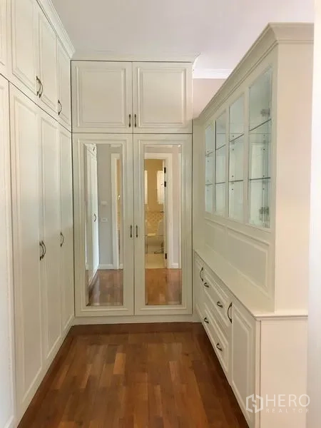 Detached House for rent in Mueang Samut Prakan, Samut Prakan - Walk‑in closet with floor‑to‑ceiling wardrobes, mirrored doors and glass‑front cabinets over wood floors.