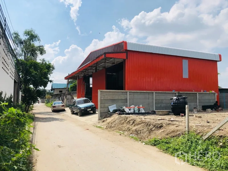 Warehouse for rent in Bang Kapi, Bangkok - Exterior of a bright red steel-clad warehouse with a pitched roof and roadside parking.