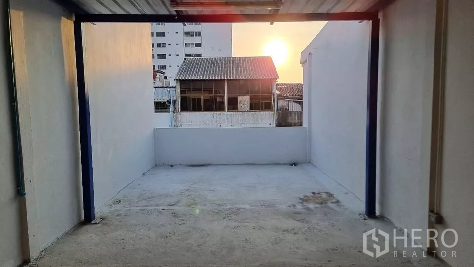 Townhouse for rent in Huai Khwang, Bangkok - Rooftop terrace with partial roof and a sunset view over low-rise buildings.
