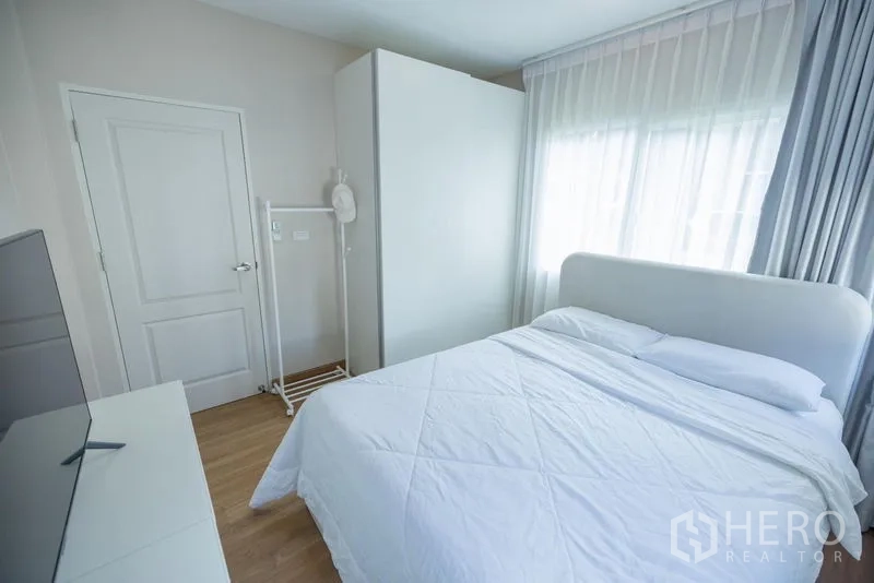 Detached House for sale in Prawet, Bangkok - Secondary bedroom with white bed, wardrobe and TV, finished with wood floors.