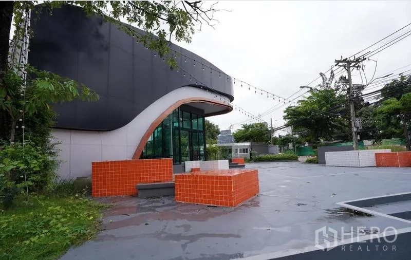 Standalone for rent in Bang Na, Bangkok - Front plaza with orange tiled seating and a curved contemporary facade.