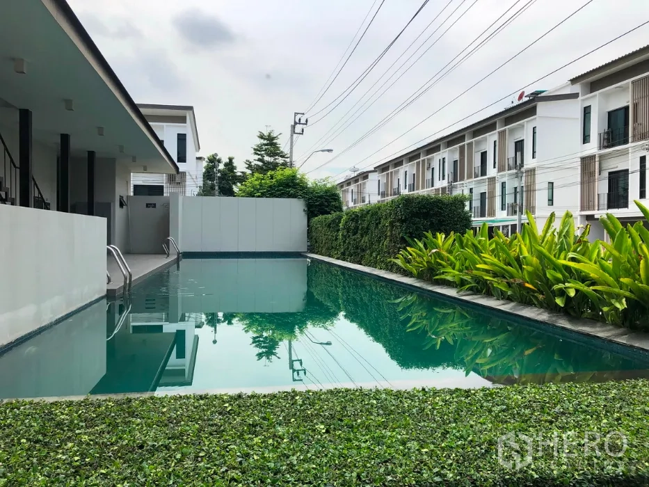 Townhouse for sale in Bang Kapi, Bangkok - Shared swimming pool bordered by tropical hedges with rows of contemporary townhomes beyond.