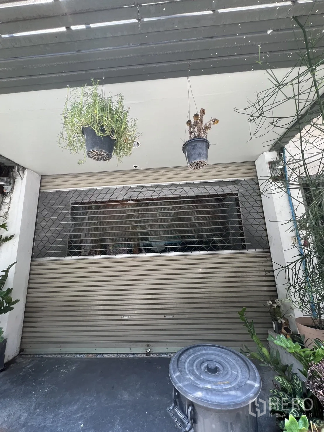 店屋 出租在Watthana, Bangkok - 一层卷帘门店面，顶部悬挂植物。
