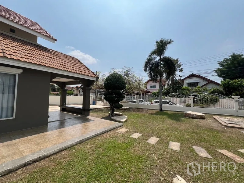 Detached House for sale in Mueang Pathum Thani, Pathum Thani - Covered terrace beside manicured topiary tree, stepping stones and a palm in the yard.