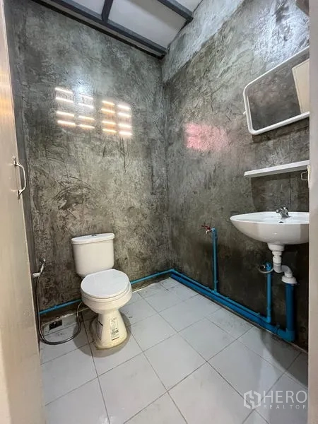 Warehouse for rent in Din Daeng, Bangkok - Warehouse restroom with toilet, sink, tiled floor, and exposed concrete walls.